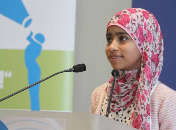 Ein junges Mädchen mit Hijab spricht an einem Rednerpult.