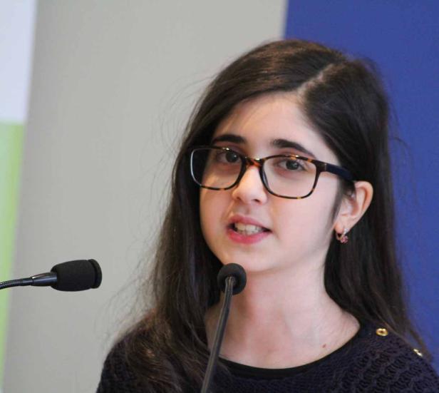 Ein junges Mädchen mit Brille spricht an einem Mikrofon.