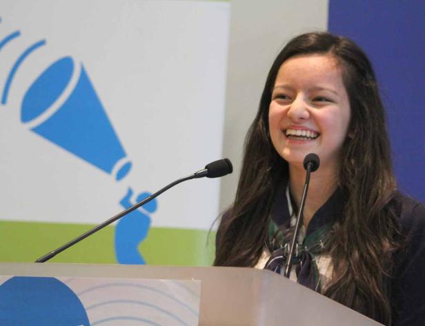 Eine junge Frau lächelt an einem Rednerpult mit Mikrofonen.