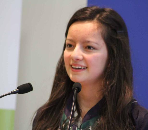 Eine junge Frau spricht bei einer Veranstaltung in ein Mikrofon.