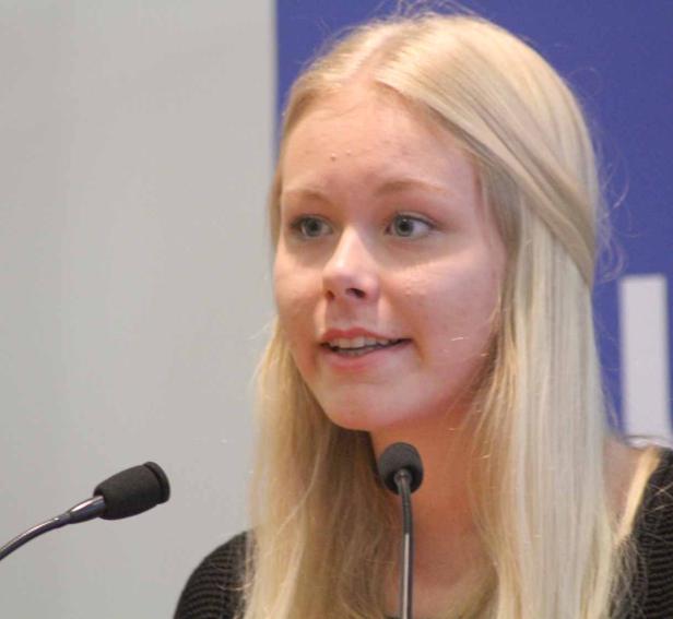 Eine junge Frau mit blonden Haaren spricht vor zwei Mikrofonen.