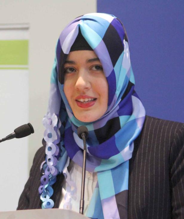 Eine junge Frau mit Hijab spricht an einem Rednerpult.