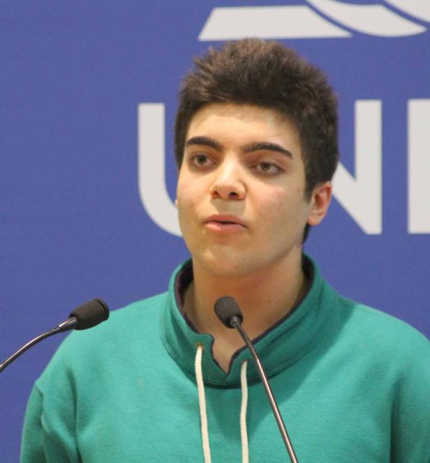 Ein junger Mann spricht vor einem blauen Hintergrund an zwei Mikrofonen.