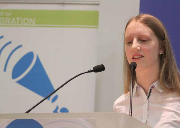 Eine junge Frau spricht bei einer Veranstaltung am Rednerpult.