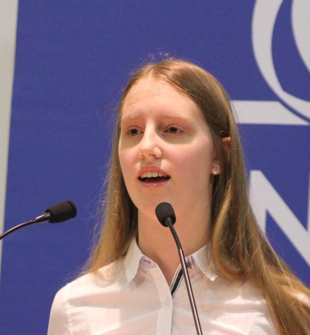 Eine junge Frau spricht vor einem Mikrofon auf einer Bühne.