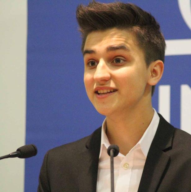 Ein junger Mann spricht bei einer Veranstaltung vor einem Mikrofon.