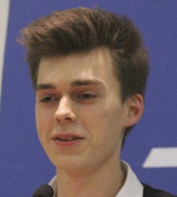 Ein junger Mann spricht vor einem blauen Hintergrund in ein Mikrofon.