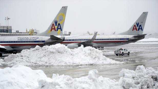 Auf einem verschneiten Flughafen stehen mehrere Flugzeuge von American Airlines.