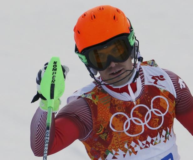 Ein Skirennläufer mit orangefarbenem Helm und Skibrille hält einen Skistock.