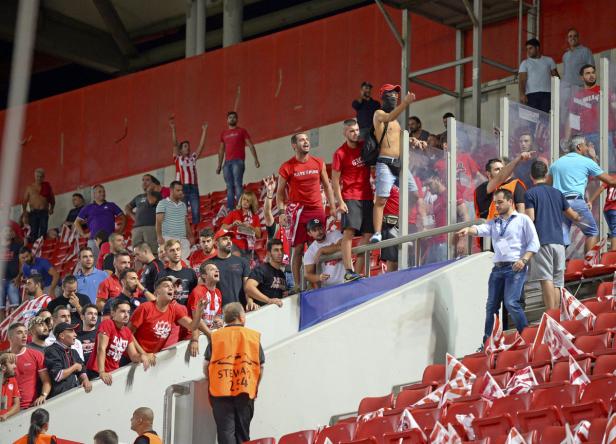 Fußballfans stehen und jubeln auf der Tribüne eines Stadions.