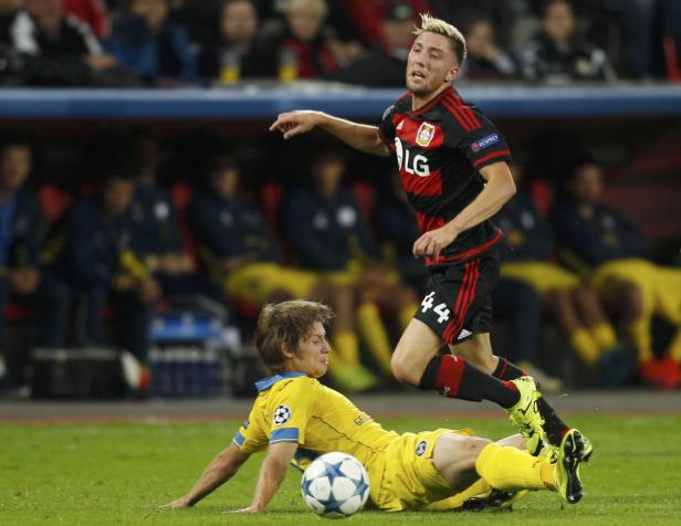 Ein Fußballspieler von Leverkusen springt über einen am Boden liegenden Spieler.