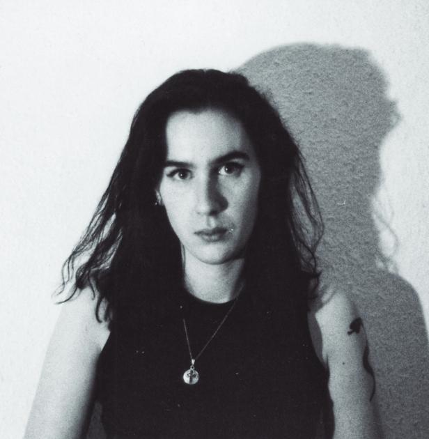 Schwarzweiß-Porträt einer jungen Frau mit dunklen Haaren und einem Tattoo am Oberarm.