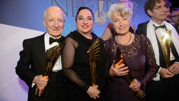 Drei Personen halten goldene Nestroy-Theaterpreise in ihren Händen.