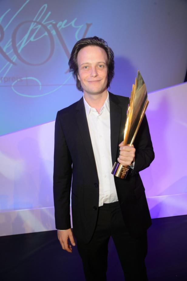 Ein Mann im Anzug hält eine goldene Trophäe in der Hand.