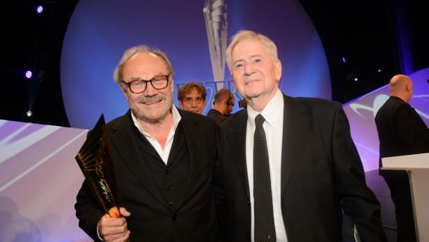 Joachim Król und Mario Adorf posieren mit einem Preis auf einer Bühne.