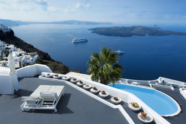Ein Pool und Liegestühle mit Blick auf das Meer und Kreuzfahrtschiffe in Santorin.