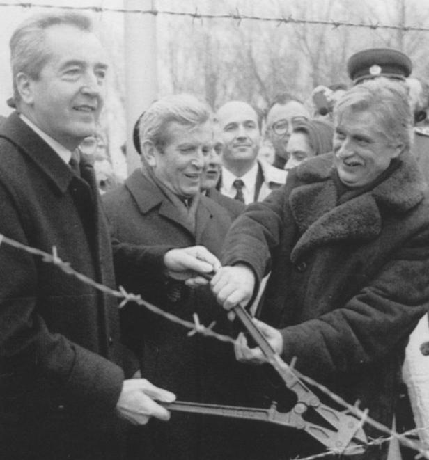 Politiker durchschneiden mit einem Bolzenschneider einen Stacheldrahtzaun.