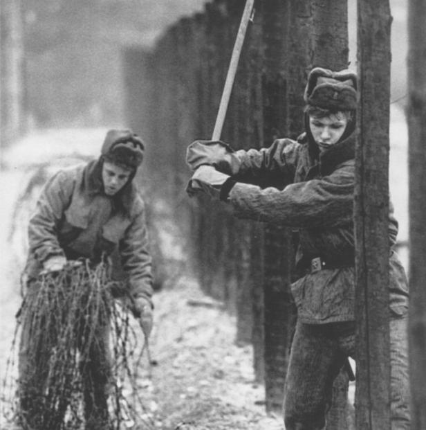 Zwei Soldaten errichten einen Stacheldrahtzaun an einer Grenze.