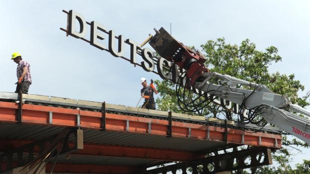Arbeiter demontieren mit einem Kran den Schriftzug „DEUTSCH“ von einem Gebäude.