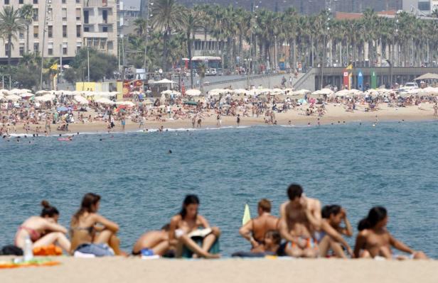 Ein belebter Strand mit vielen Menschen und Sonnenschirmen an einem sonnigen Tag.