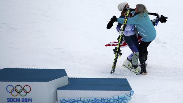 Eine Skifahrerin umarmt eine Frau vor dem Siegerpodest bei den Olympischen Winterspielen 2014 in Sotschi.