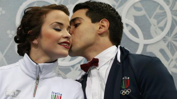 Ein italienisches Eiskunstlaufpaar umarmt sich vor dem Hintergrund der Olympischen Ringe.