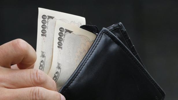 Eine Hand hält einen schwarzen Geldbeutel mit mehreren 10.000-Yen-Scheinen.