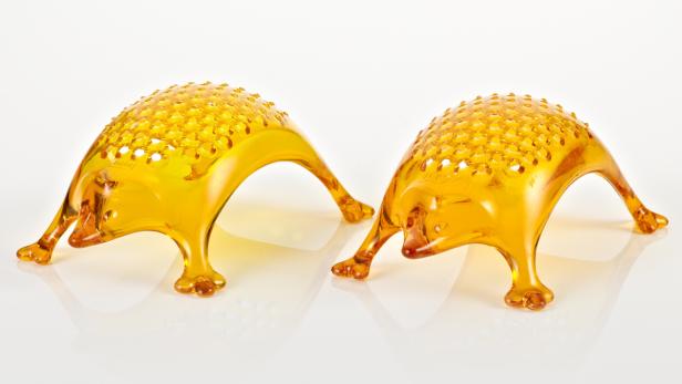 Zwei dekorative, bernsteinfarbene Igel aus Kunststoff stehen auf einer glänzenden Oberfläche.