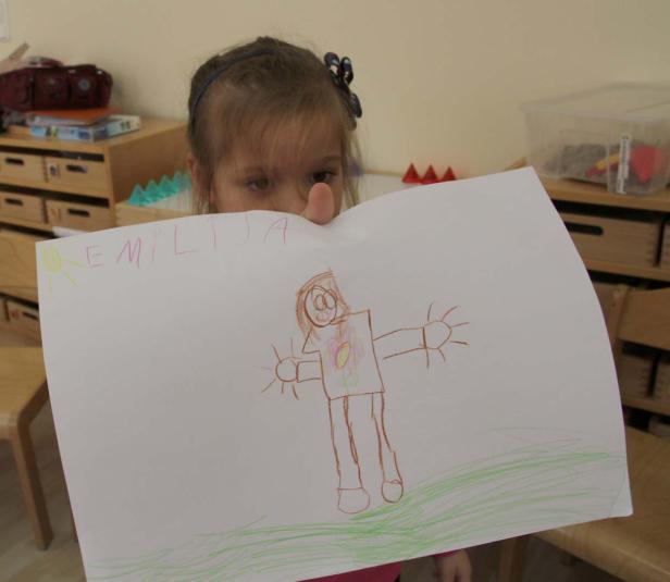 Ein Mädchen zeigt ein selbstgemaltes Bild mit dem Namen „Emilija“.