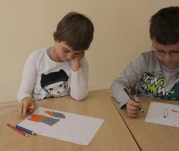 Zwei Kinder sitzen an einem Tisch und malen Bilder mit Stiften.