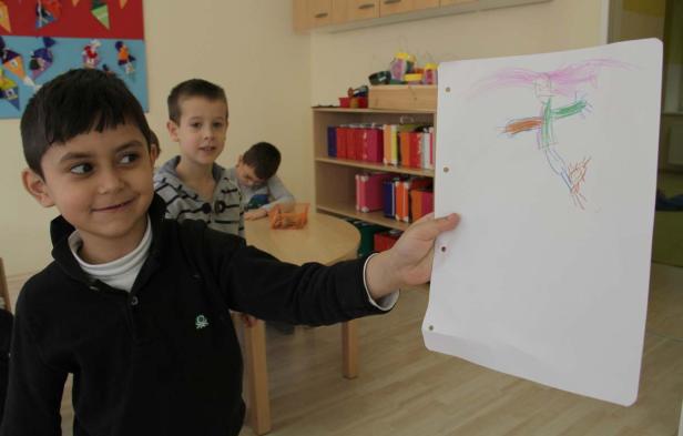 Ein Junge präsentiert stolz eine Zeichnung mit bunten Stiften vor anderen Kindern.