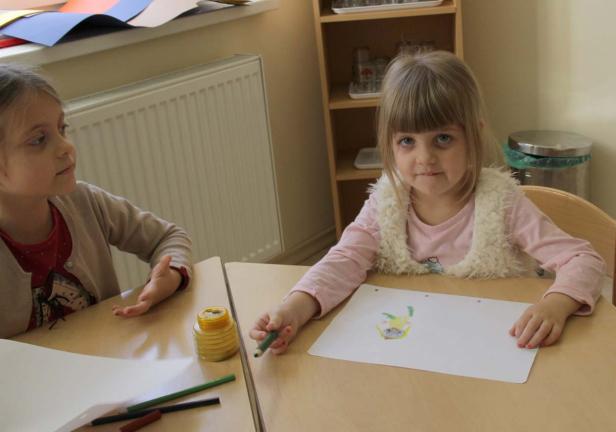 Ein Mädchen malt mit Buntstiften auf einem Blatt Papier.