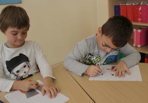 Zwei Kinder sitzen an einem Tisch und malen Bilder.