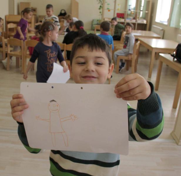 Ein Junge präsentiert stolz eine Zeichnung in einem Klassenzimmer.