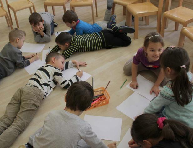 Eine Gruppe Kinder liegt auf dem Boden und malt mit Buntstiften auf Papier.
