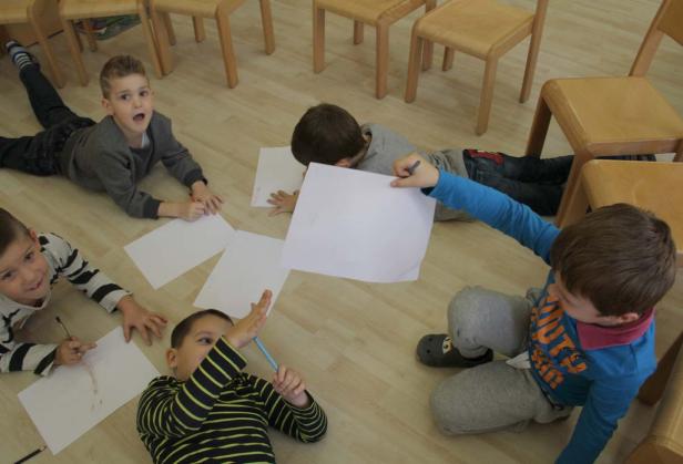 Eine Gruppe von Kindern liegt auf dem Boden und malt oder zeichnet auf Papier.