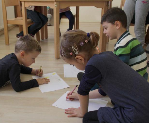 Drei Kinder sitzen auf dem Boden und malen mit Stiften auf Papier.