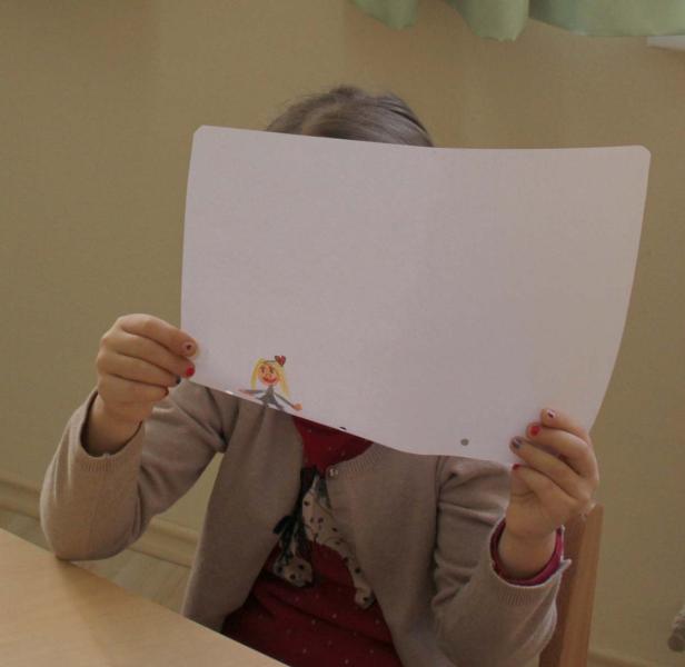 Ein Kind hält ein Blatt Papier mit einer Zeichnung vor sein Gesicht.