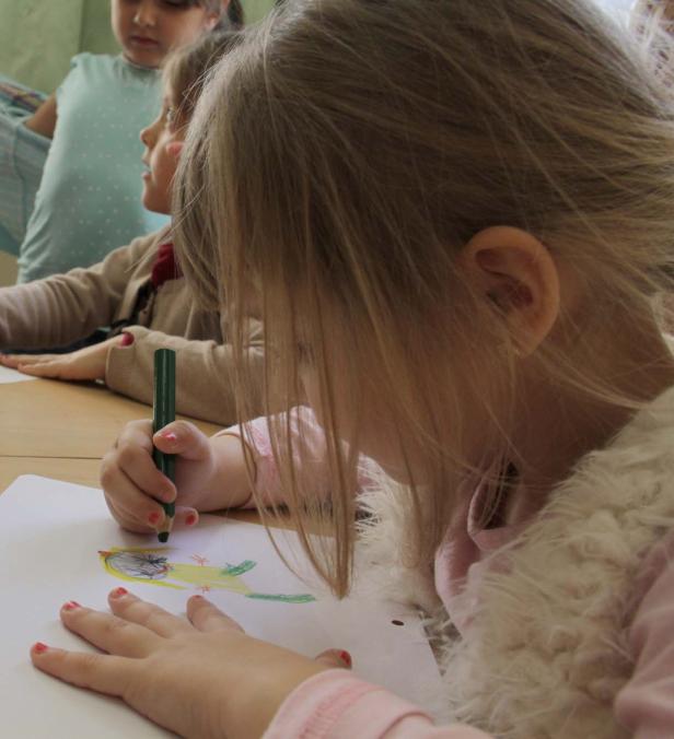 Ein Mädchen zeichnet mit einem grünen Stift auf ein Blatt Papier.