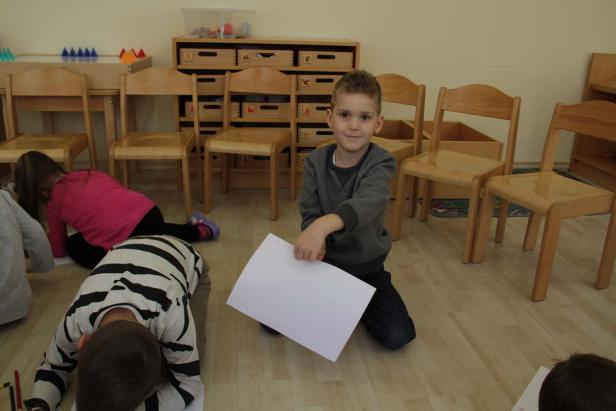 Ein Junge kniet mit einem Blatt Papier in einem Klassenzimmer.