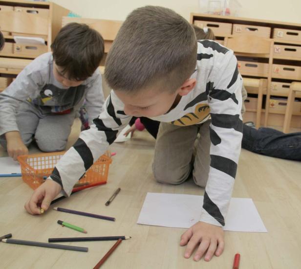 Kinder sitzen auf dem Boden und malen mit Buntstiften.