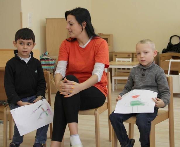 Eine Frau sitzt mit zwei kleinen Jungen in einem Raum, die ihre Zeichnungen präsentieren.