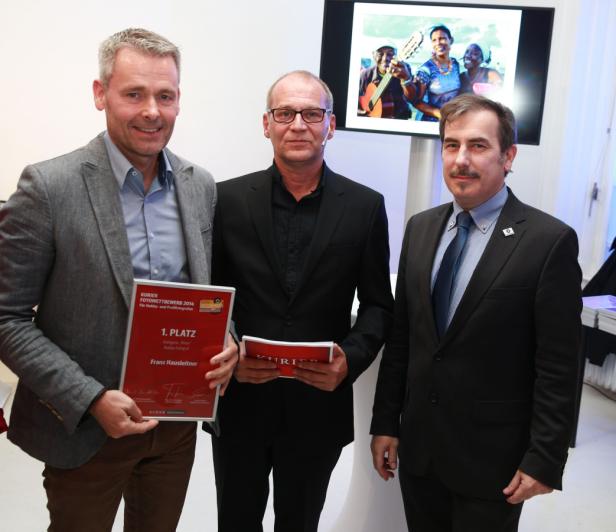 Drei Männer posieren mit einer Urkunde für den „Kurier Fotowettbewerb 2014“.