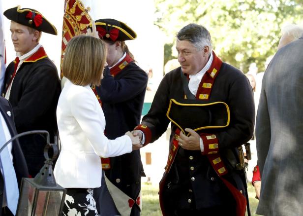 Eine Frau im weißen Blazer schüttelt einem Mann in historischer Uniform die Hand.