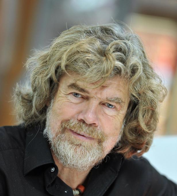 Reinhold Messner mit grauem, lockigem Haar und Bart lächelt in die Kamera.