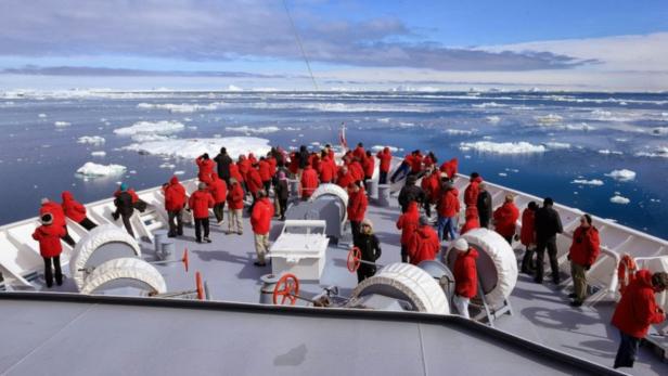 Eine Gruppe von Menschen in roten Jacken steht auf dem Deck eines Schiffes in der Antarktis.