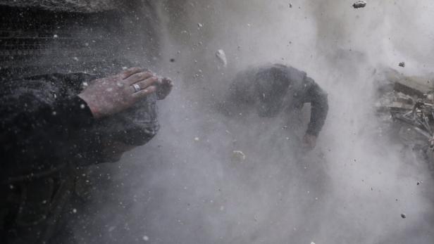 Zwei Personen ducken sich inmitten von Staub und Trümmern.