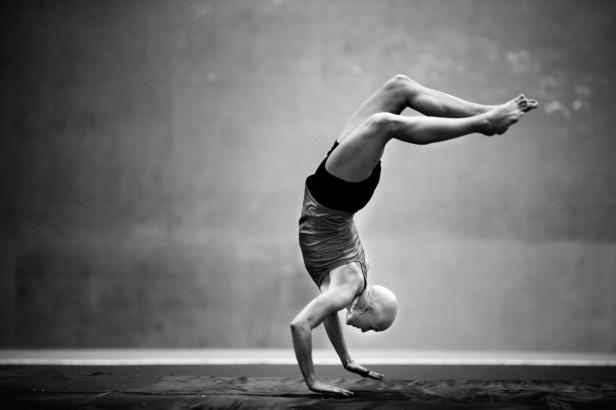 Eine Frau macht einen Handstand vor einer grauen Wand.