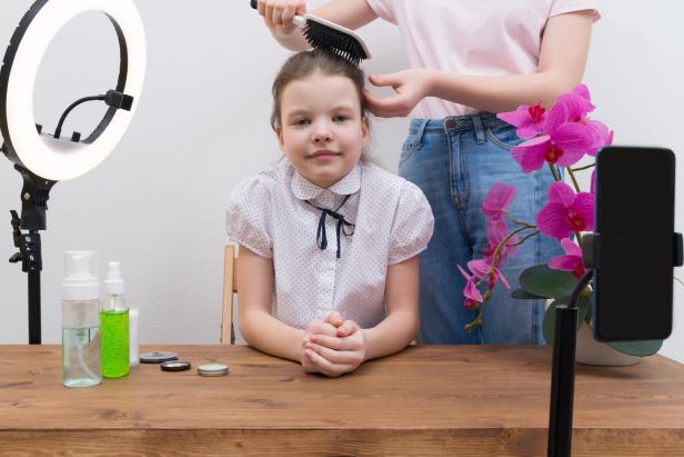 Ein Mädchen sitzt am Tisch, während eine andere Person ihr die Haare bürstet.