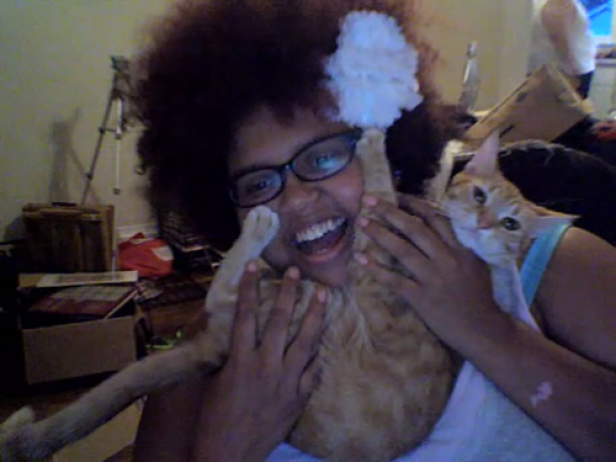 Eine lachende Frau mit Brille hält eine orangefarbene Katze im Arm.